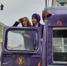 two women standing in the drivers seat of a purple truck, looking out the window