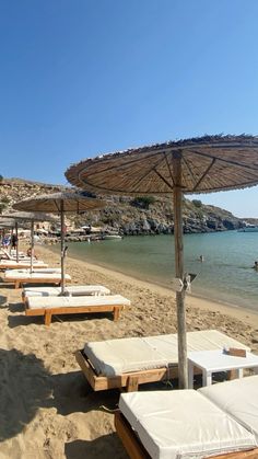 lounge chairs and umbrellas are on the beach near the water with people swimming in the ocean