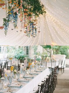 the tables are set with place settings and flowers hanging from the ceiling in front of them