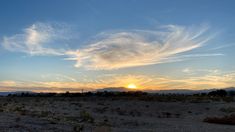 the sun is setting over an arid area with mountains in the distance and clouds in the sky