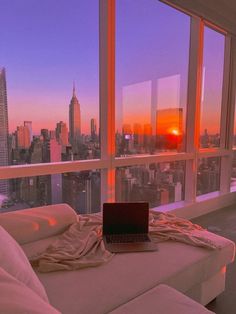 a laptop computer sitting on top of a white couch in front of a large window