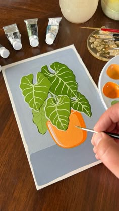 a person is painting an orange and green plant on a piece of paper with acrylic paint