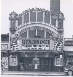 an old theater with cars parked in front of it and advertisements on the side of the building