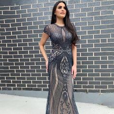 a woman standing in front of a brick wall wearing a dress with an intricate pattern