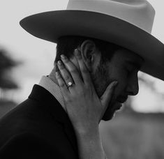 a man in a cowboy hat holding his hand to his face