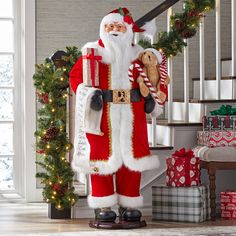 a santa clause holding a teddy bear in front of christmas decorations and presents on the stairs