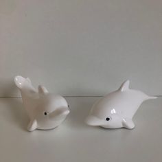 two white ceramic dolphin figurines sitting on a counter top next to each other