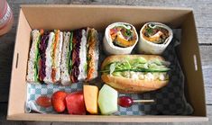 a box filled with sandwiches and fruit on top of a wooden table next to a drink