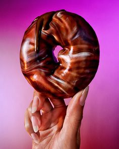 a hand holding a chocolate donut in front of a purple background