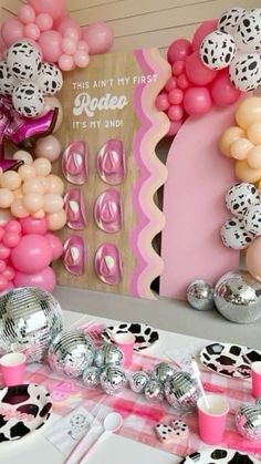 a table topped with lots of pink and white balloons next to a wall covered in cow print