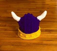 a purple and yellow knitted hat with white horns on the top sitting on a wooden floor