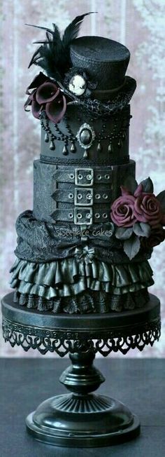 a three tiered cake decorated with black and pink flowers on a metal stand in front of a wall