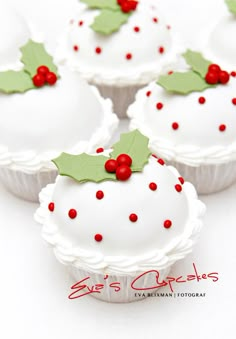 four cupcakes decorated with holly leaves and red berries on white frosted paper