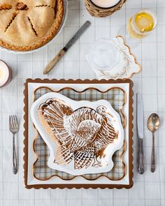 a turkey cut out on a plate next to a pie and candlelight holder with utensils