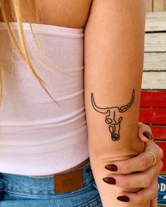 a woman's arm with a tattoo of a bull skull on it and a name tag