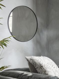 a round mirror hanging on the wall next to a black couch with white and grey pillows