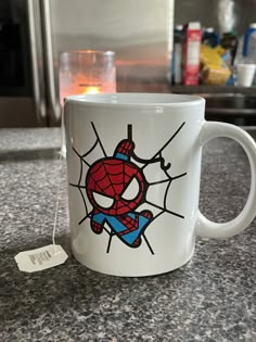 a spiderman mug sitting on top of a counter next to a cup with a tag