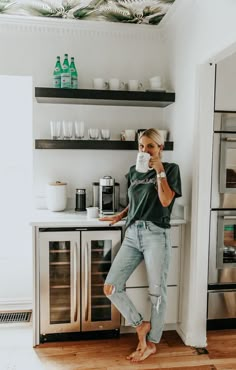 a woman standing in the kitchen drinking from a cup