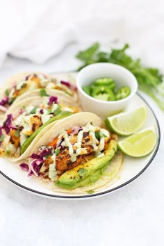 three fish tacos on a plate with limes and cilantro