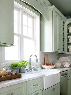 a kitchen filled with lots of green cabinets and white counter tops next to a window