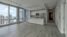 an empty kitchen and living room in a large apartment with floor to ceiling windows overlooking the city