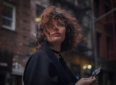 a woman with curly hair holding a cell phone in her hand and looking off to the side