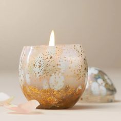 a candle that is sitting next to some glass balls on a white surface with gold flecks