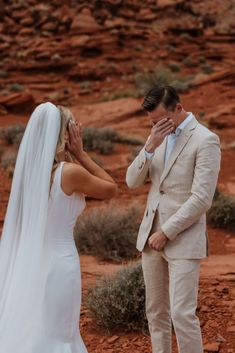 a man and woman in wedding attire standing next to each other with their hands covering their eyes