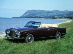 an old car is parked on the grass by the water