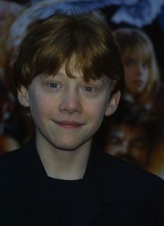 a young boy with brown hair and blue eyes smiles at the camera while standing in front of a movie poster