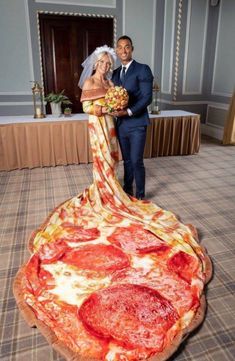 a bride and groom posing in front of a giant pizza