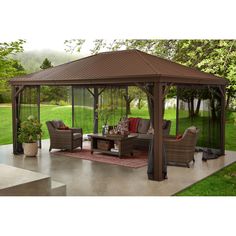 a gazebo sitting on top of a patio next to a lush green field and trees