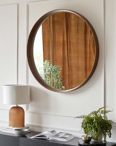 a round mirror hanging on the side of a wall next to a lamp and table