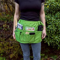 a woman standing in front of bushes holding a baseball bat and some other items inside her pocket