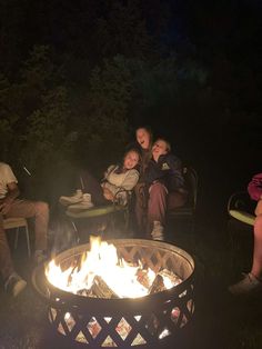 people sitting around a fire pit in the dark with their arms wrapped around each other