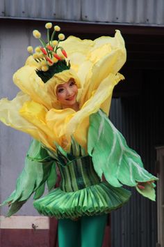 a woman dressed in green and yellow holding a large flower