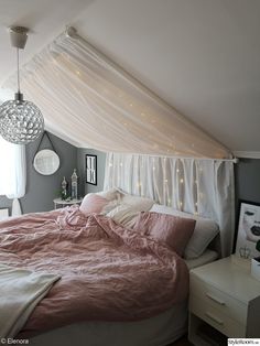 a bed that has some lights on the headboard and curtains over it in a bedroom