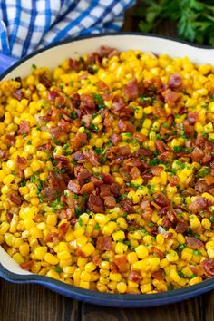 corn with bacon and parsley in a white dish on a wooden table next to a blue towel