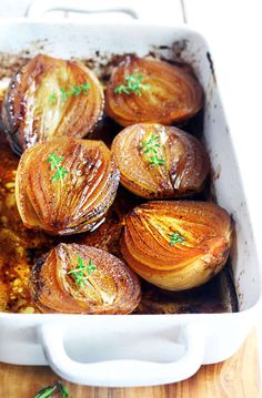 some onions are in a white casserole dish on a wooden table with parsley