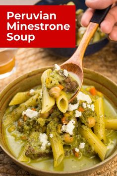 a wooden spoon filled with pasta and broccoli in a green sauce on top of a table