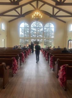 a woman walking down the aisle of a church with red bows on it's pews