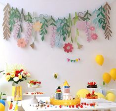 a birthday party with paper flowers, balloons and cake on a table in front of a white wall