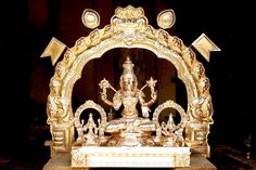 an ornate gold statue is displayed on a wooden platform in front of a black background