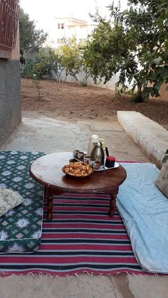 a table that has food on it in the middle of a yard with a blanket