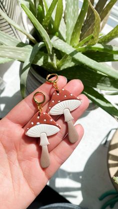 a person holding up two small keychains in front of a potted plant