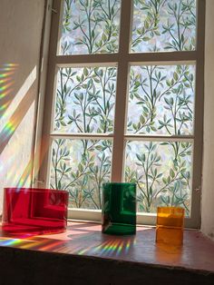 the sun shines through two windows in a room with colorful vases on display