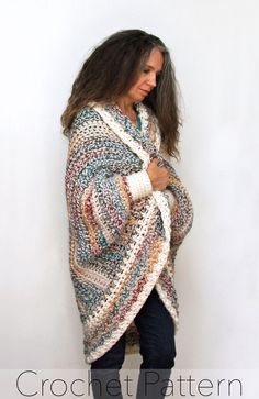 a woman wearing a multicolored crochet shawl standing against a white wall