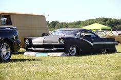 an old car is parked in the grass near other cars and trucks at a car show