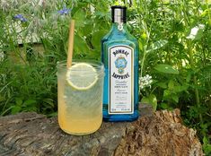 a bottle of lemonade next to a glass on a tree stump