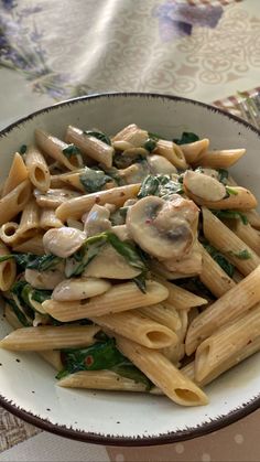 a white bowl filled with pasta covered in mushrooms and spinach leaves on top of a table